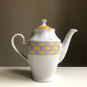 Könnte beinhalten: Weiße Keramik-Teekanne mit einem geometrischen Muster in Gelb und Braun. Die Teekanne hat einen Deckel und einen Griff.