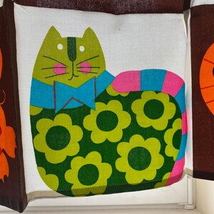 May include: A green cat with a blue bow tie and pink and blue tail, wearing a green and yellow floral pattern. The cat is on a white background.