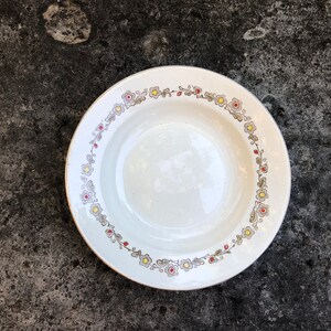 以下が含まれることがあります： 赤、黄、グレーの色合いの花柄が施された白いセラミック製のスープボウル。ボウルは金色の縁取りが施されています。