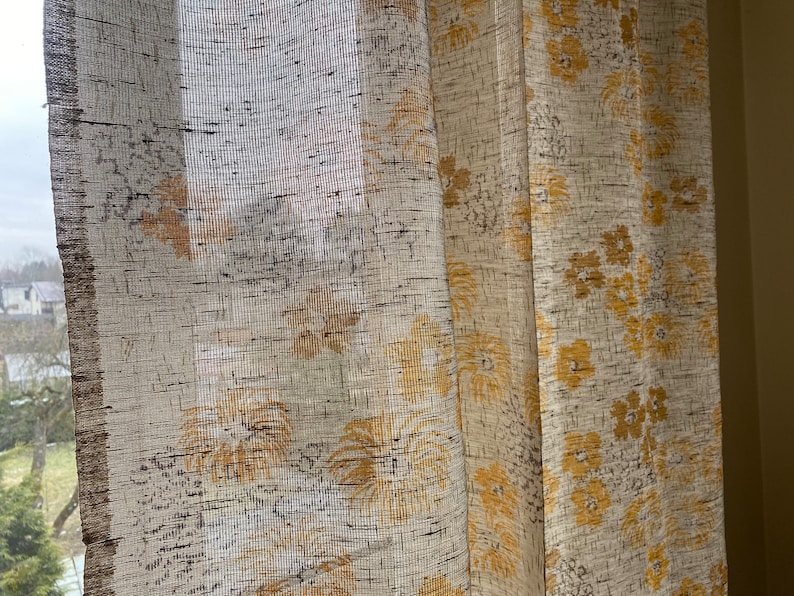 May include: A pair of sheer curtains with a floral pattern in shades of beige and yellow.