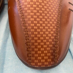 May include: Close-up of a brown leather shoe with a checkered pattern on the side.