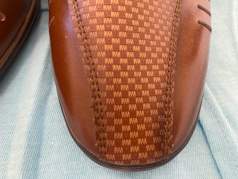 May include: Close-up of a brown leather shoe with a checkered pattern on the side.