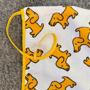 May include: White cotton towel with a yellow border and a repeating pattern of yellow cartoon dogs. The towel has a yellow drawstring.