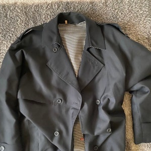 Op de afbeelding: Een zwarte dubbelrijdige trenchcoat met een geruite voering.