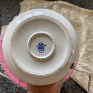 Może przedstawiać: Biała ceramiczna podstawa lampy z niebiesko-białym logo z napisem "Unter Weiss Bach" i r&oacute;żową koronkową ozdobą wok&oacute;ł podstawy.