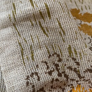 May include: Close-up of a beige fabric with a woven texture. The fabric has a pattern of brown and yellow leaves.