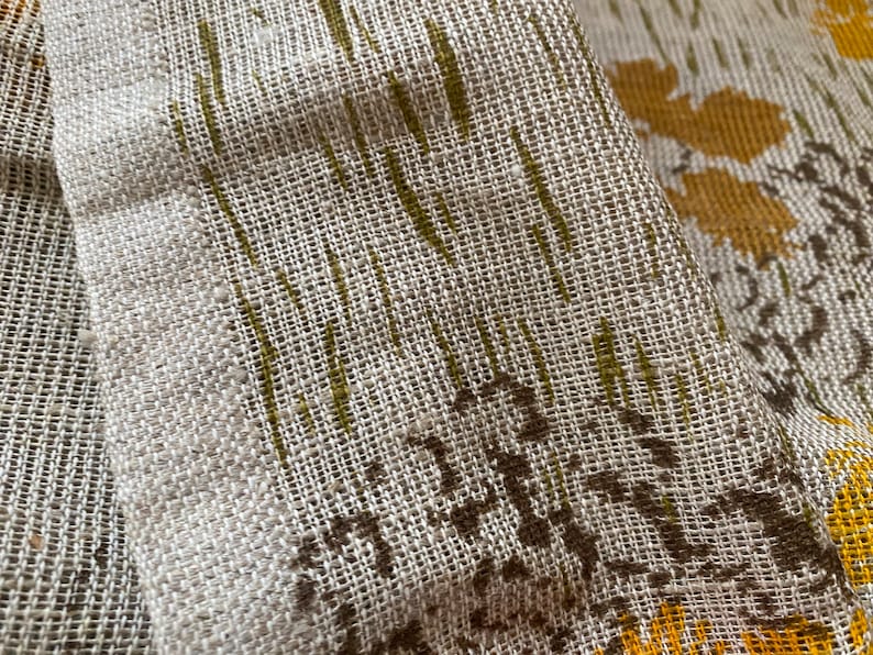 May include: Close-up of a beige fabric with a woven texture. The fabric has a pattern of brown and yellow leaves.