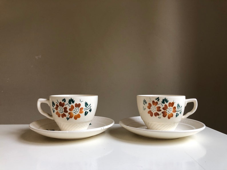 Peut inclure: Deux tasses &agrave; th&eacute; blanches avec des motifs floraux marrons et verts et des soucoupes assorties.