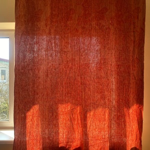 May include: A red patterned curtain hangs in a window, with sunlight shining through the fabric, creating a warm and inviting atmosphere.