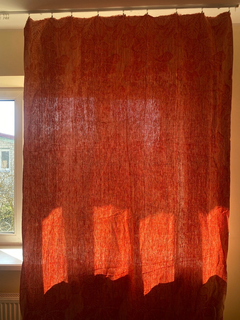 May include: A red patterned curtain hangs in a window, with sunlight shining through the fabric, creating a warm and inviting atmosphere.