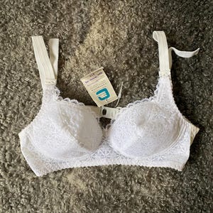Puede incluir: Sujetador de encaje blanco con tirantes ajustables y cierre de gancho y ojo en la espalda. El sujetador tiene un delicado patrón floral y está hecho de un material suave y cómodo.