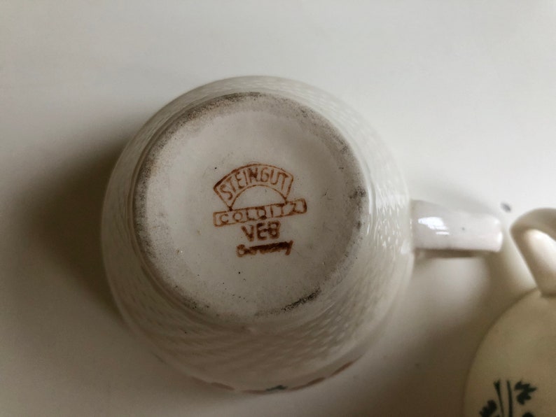 Peut inclure: Gros plan du fond d'une tasse &agrave; th&eacute; en c&eacute;ramique blanche avec un logo brun qui indique "Steingut Colditz VEB Germany".
