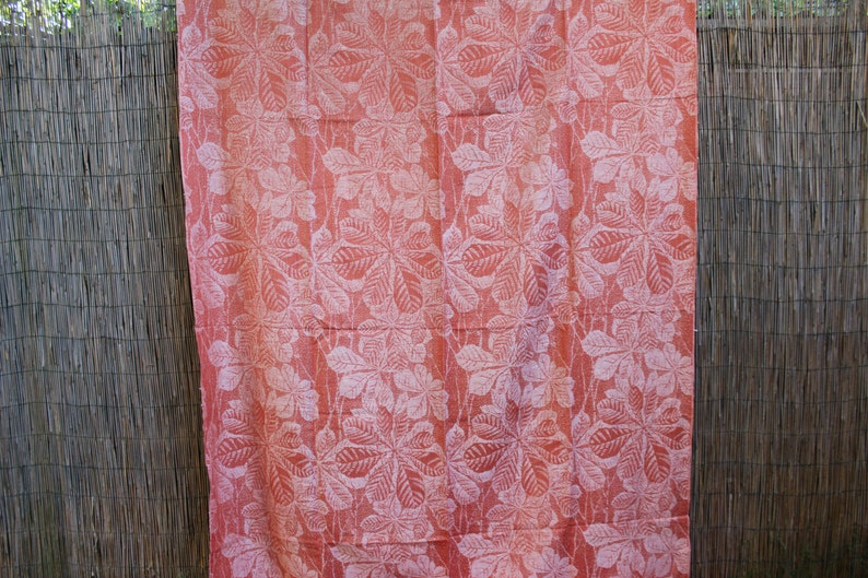 May include: A pink fabric with a white leaf pattern. The fabric is hanging on a woven fence.