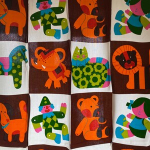 May include: A colorful fabric panel with a repeating pattern of animals and figures. The panel features a dog, a horse, an elephant, a cat, a lion, a clown, and a teddy bear. The panel is made of a white fabric with brown squares.