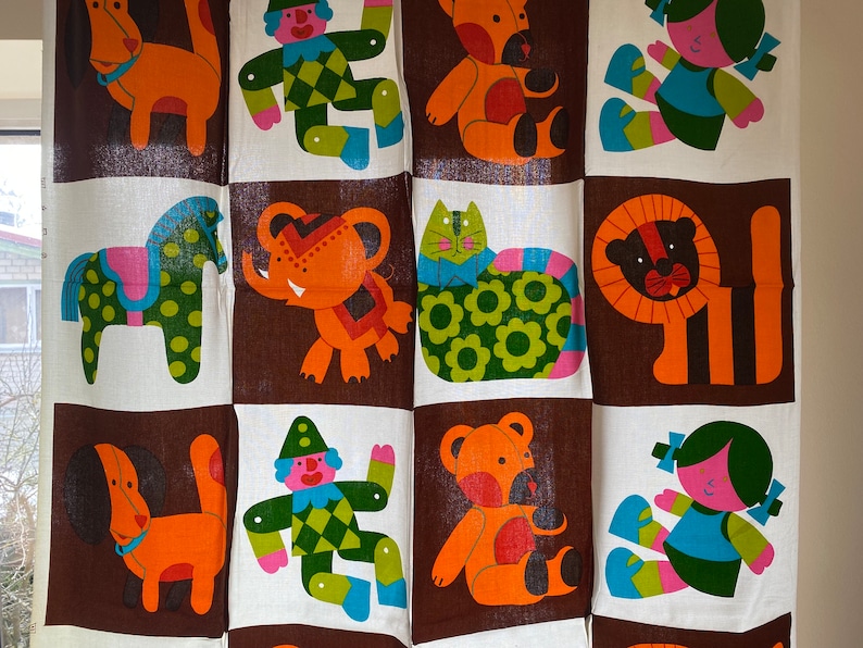 May include: A colorful fabric panel with a repeating pattern of animals and figures. The panel features a dog, a horse, an elephant, a cat, a lion, a clown, and a teddy bear. The panel is made of a white fabric with brown squares.