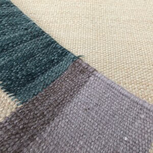 May include: Close-up of a woven rug with a geometric pattern in shades of beige, brown, gray, and teal.