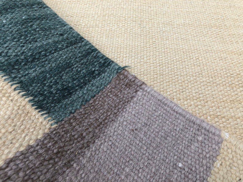 May include: Close-up of a woven rug with a geometric pattern in shades of beige, brown, gray, and teal.