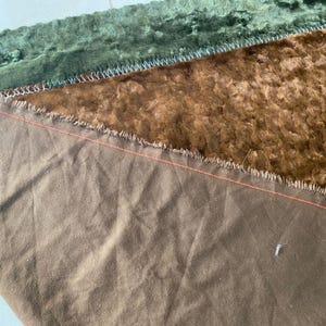 May include: Close-up of a brown fabric with a frayed edge. The fabric is sewn to a green fabric with a similar frayed edge.