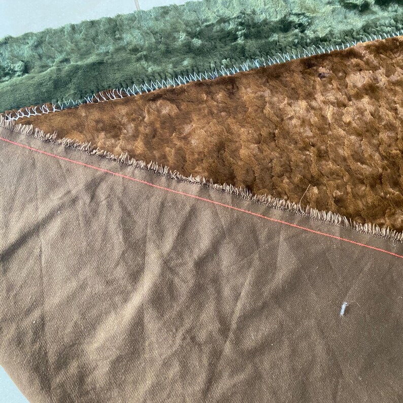 May include: Close-up of a brown fabric with a frayed edge. The fabric is sewn to a green fabric with a similar frayed edge.
