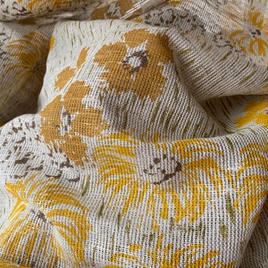 May include: Close-up of a white fabric with a yellow floral pattern. The fabric has a textured, woven appearance.