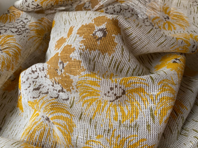 May include: Close-up of a white fabric with a yellow floral pattern. The fabric has a textured, woven appearance.