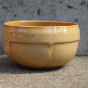 May include: A light brown ceramic bowl with a rounded shape and a slightly textured surface. The bowl has a smooth, glossy finish and is perfect for serving snacks or salads.