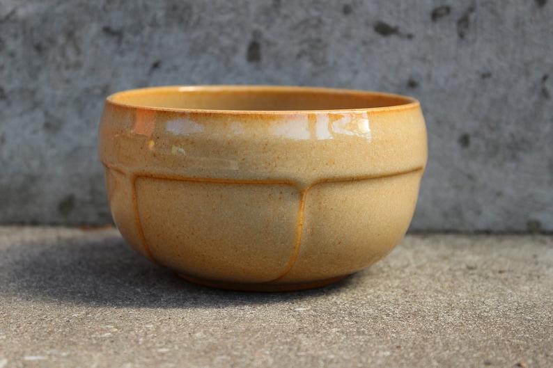 May include: A light brown ceramic bowl with a rounded shape and a slightly textured surface. The bowl has a smooth, glossy finish and is perfect for serving snacks or salads.