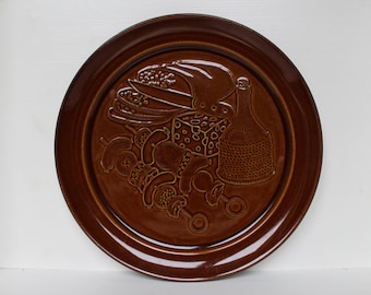 May include: A brown ceramic serving plate with a raised design of a skewer of food, a bottle of wine, and a piece of cheese.