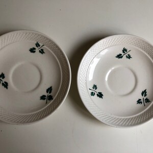 Peut inclure: Deux soucoupes en c&eacute;ramique blanche avec un motif tiss&eacute; et des motifs de feuilles vertes.