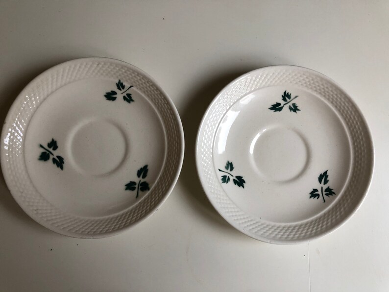 Peut inclure: Deux soucoupes en c&eacute;ramique blanche avec un motif tiss&eacute; et des motifs de feuilles vertes.