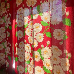 Könnte beinhalten: Rote Vorhänge mit einem weißen Gänseblümchen-Blumenmuster. Die Vorhänge sind aus einem leichten Stoff gefertigt und haben eine durchscheinende Textur.