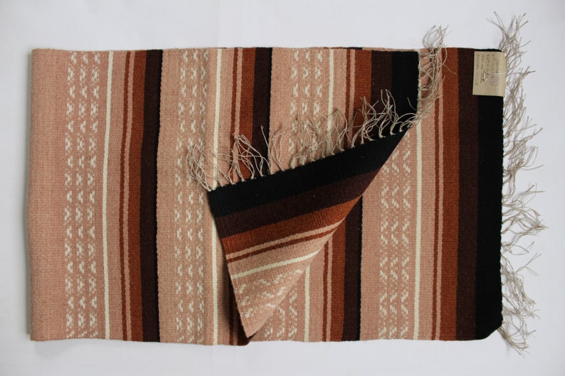 May include: A woven rug with a striped pattern in shades of brown, pink, and white. The rug has a fringe border and is folded in half.