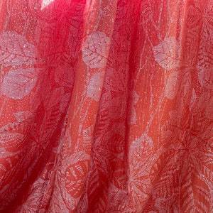 May include: A close-up of a red fabric with a white floral pattern. The fabric is sheer and has a slightly shimmery finish.