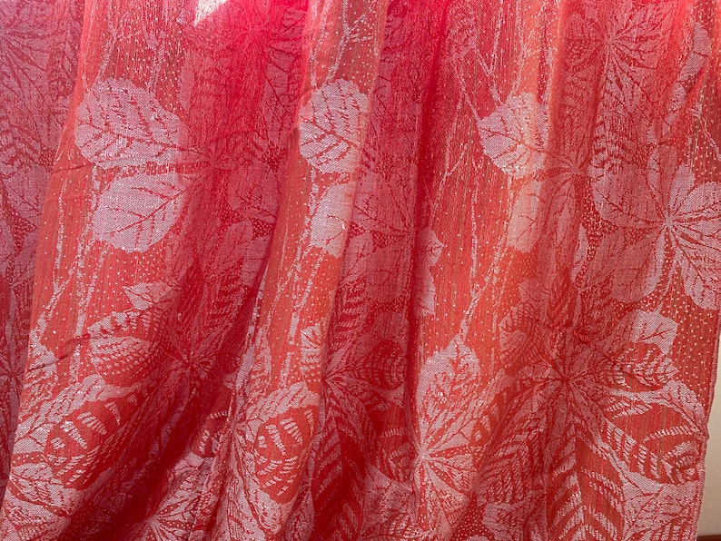 May include: A close-up of a red fabric with a white floral pattern. The fabric is sheer and has a slightly shimmery finish.