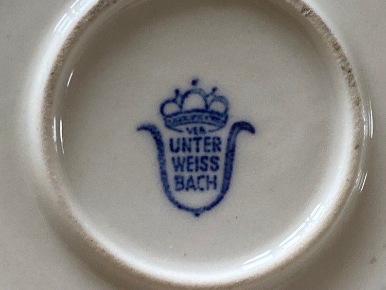 Może przedstawiać: Niebiesko-biały znak porcelanowy z koroną i tekstem "Unter Weiss Bach" na białym tle.