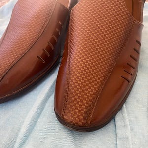 May include: A pair of brown leather slip-on shoes with a checkered pattern. The shoes have a pointed toe and a small heel.