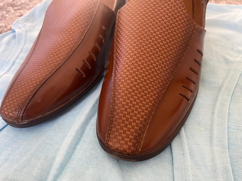 May include: A pair of brown leather slip-on shoes with a checkered pattern. The shoes have a pointed toe and a small heel.