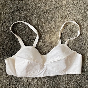 Op de afbeelding: Witte katoenen bh met verstelbare bandjes en een delicaat bloemenpatroon. De bh is zacht, comfortabel en heeft een klassiek ontwerp.