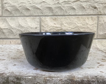 May include: A black ceramic bowl with a smooth, glossy finish. The bowl is empty and sits on a light gray surface.