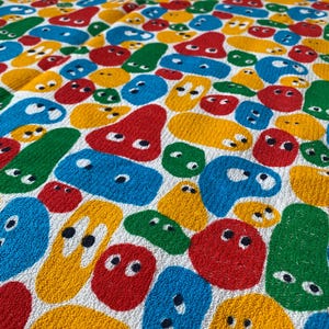 Pu&ograve; includere: Un tessuto bianco con un motivo ripetuto di forme astratte colorate. Le forme sono rosse, gialle, blu e verdi, ognuna con due piccoli punti neri che assomigliano a occhi. Il design &egrave; giocoso e vibrante.