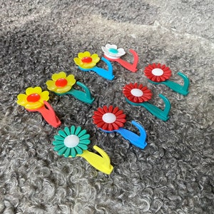 May include: Assortment of colorful flower-shaped hooks with a white center. The hooks are made of plastic and have a spring-loaded mechanism. They are perfect for hanging lightweight items.