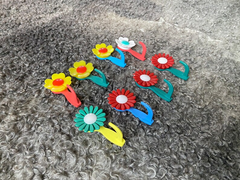 May include: Assortment of colorful flower-shaped hooks with a white center. The hooks are made of plastic and have a spring-loaded mechanism. They are perfect for hanging lightweight items.