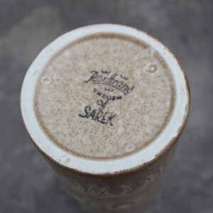 K&ouml;nnte beinhalten: Der Boden einer wei&szlig;en Keramikvase mit brauner Glasur. Die Vase ist mit dem Text "R&ouml;rstrand Sweden" und "SAREK" gekennzeichnet.