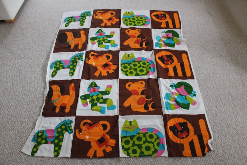 May include: A brown and white fabric with a repeating pattern of colorful animals. The animals include a horse, elephant, cat, lion, dog, and a clown. The fabric is perfect for a baby quilt or other sewing projects.