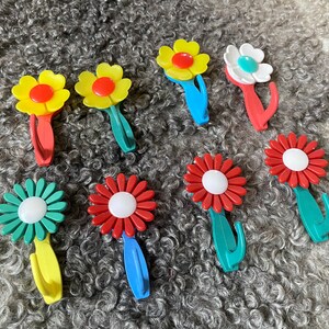 May include: Nine colorful flower-shaped hooks with a white center. The hooks are made of plastic and have a retro design.
