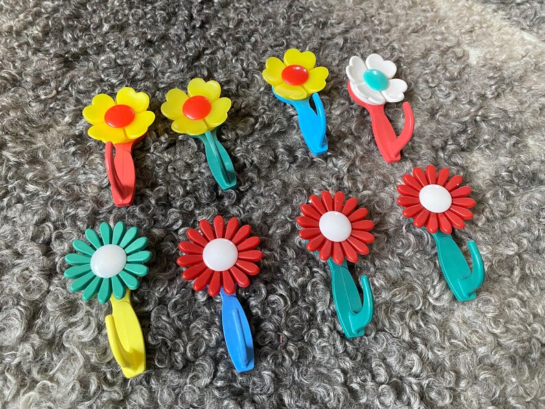 May include: Nine colorful flower-shaped hooks with a white center. The hooks are made of plastic and have a retro design.