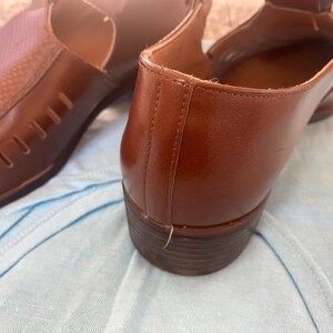 May include: A pair of brown leather shoes with cutouts. The shoes have a pointed toe and a low heel.
