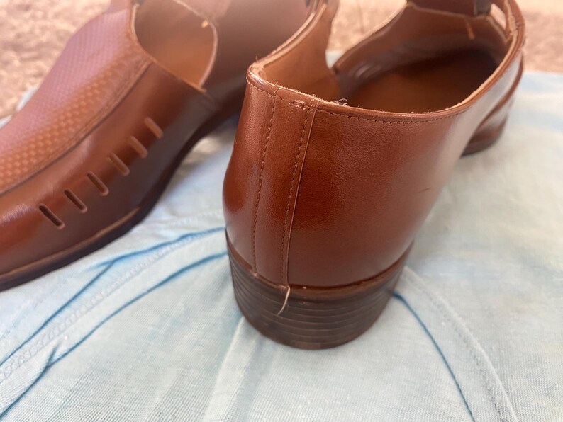 May include: A pair of brown leather shoes with cutouts. The shoes have a pointed toe and a low heel.