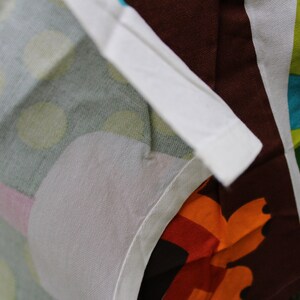 May include: A white fabric with a colorful pattern of circles, flowers, and a cat. The fabric has a white border and is folded in half.