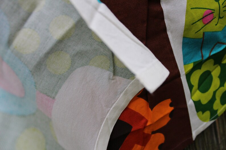 May include: A white fabric with a colorful pattern of circles, flowers, and a cat. The fabric has a white border and is folded in half.